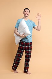 Photo of Happy man in pyjama holding pillow on beige background