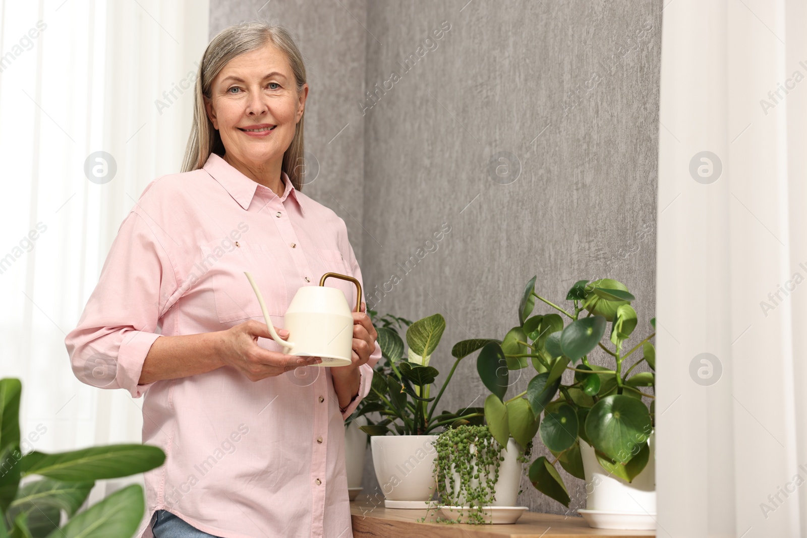 Photo of Happy housewife with watering can near green houseplants at home