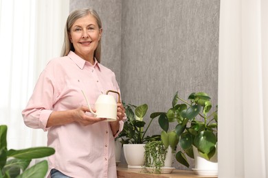 Happy housewife with watering can near green houseplants at home