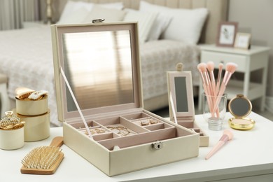 Photo of Elegant jewelry box with beautiful bijouterie and cosmetics on dressing table in bedroom