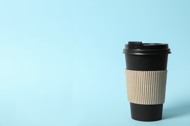 Photo of Takeaway paper coffee cup with cardboard sleeve on light blue background. Space for text