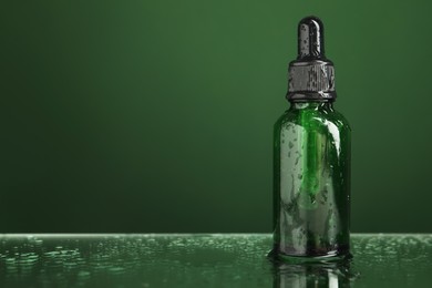 Photo of Bottle of face serum on wet surface against green background, closeup. Space for text