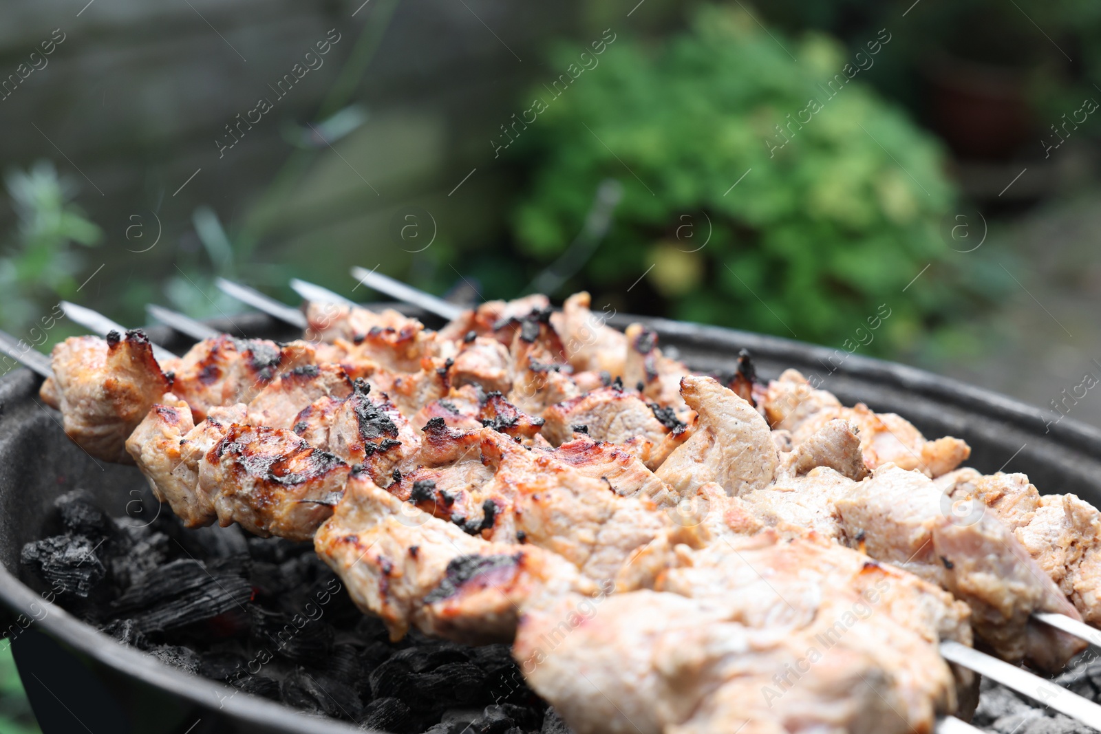 Photo of Cooking delicious kebab on metal brazier outdoors, closeup