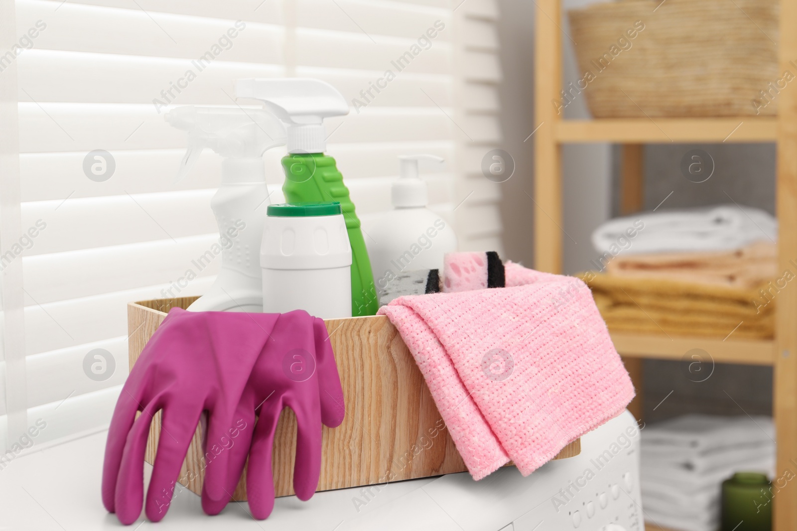 Photo of Different cleaning products in wooden box on washing machine indoors