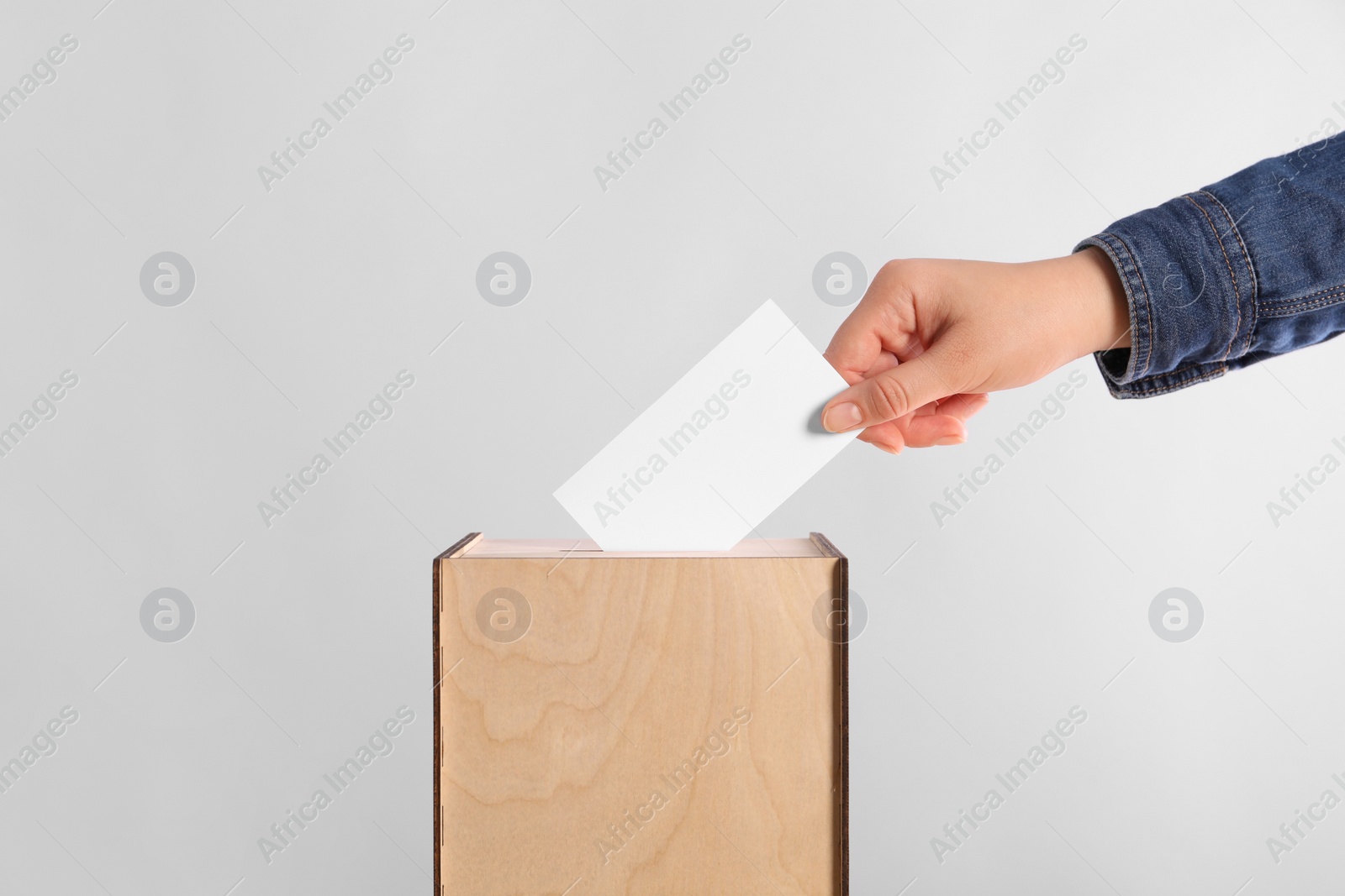 Photo of Woman putting her vote into ballot box on light grey background, closeup