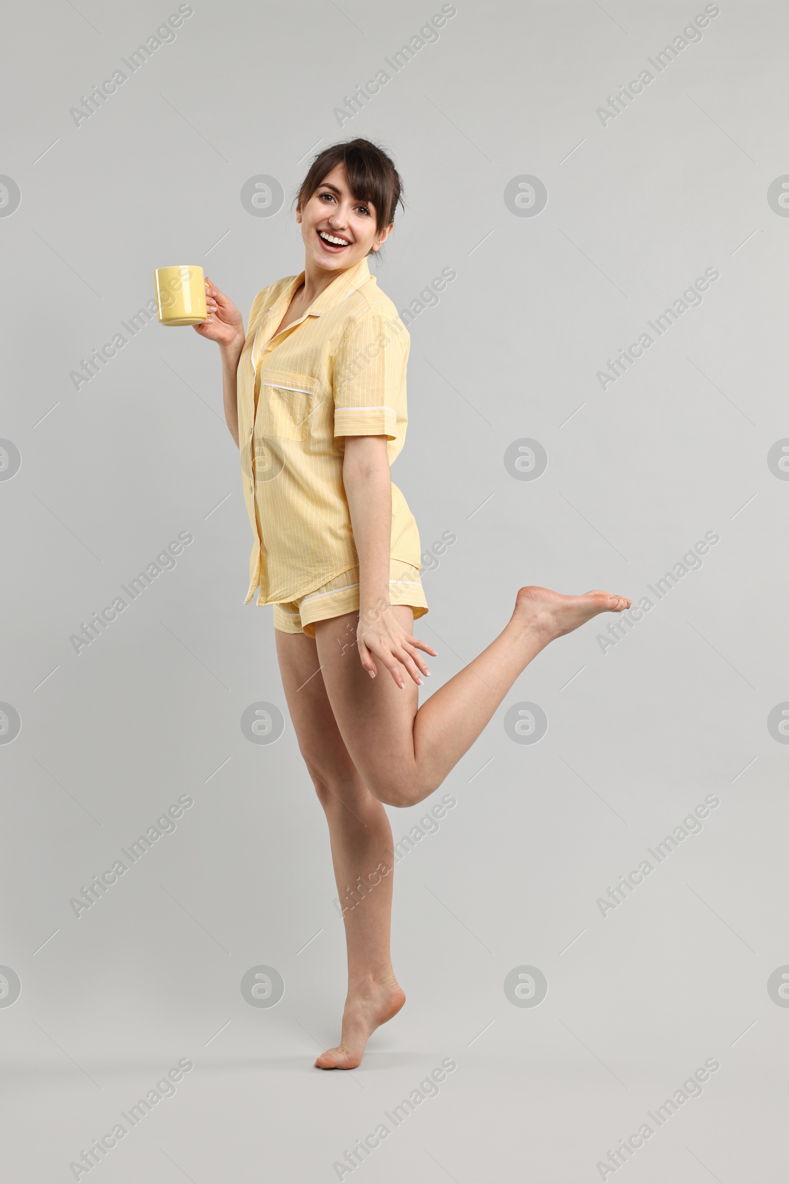 Photo of Happy woman in pyjama holding cup of drink on grey background