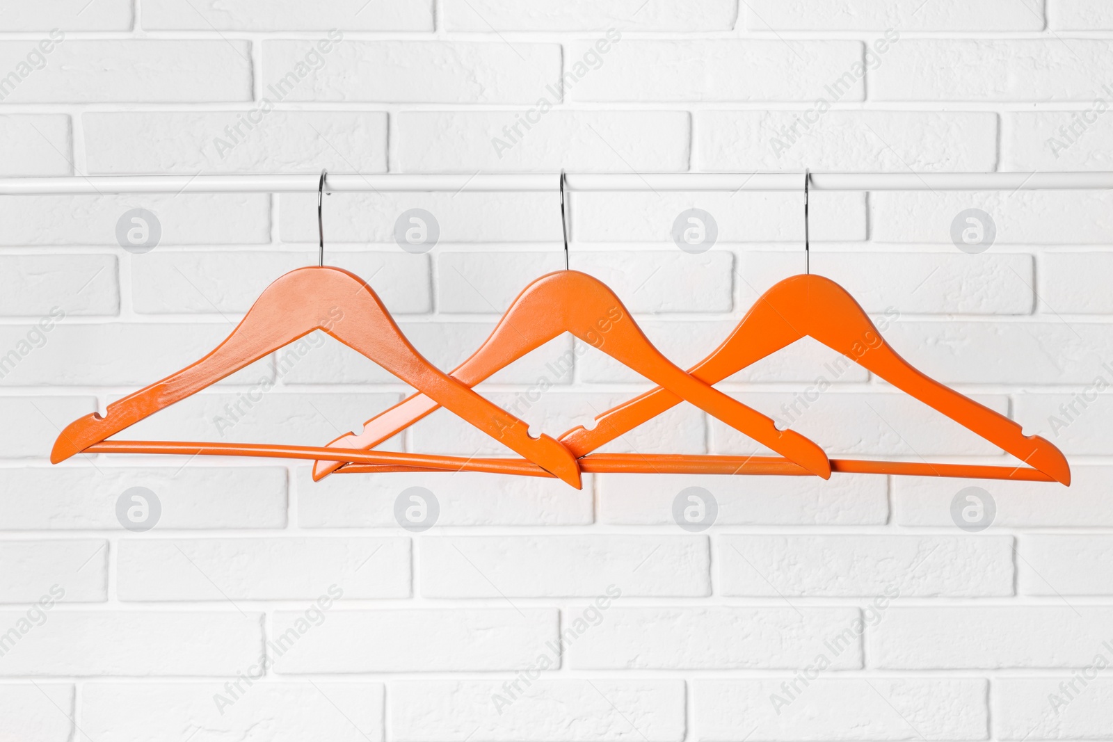 Photo of Orange clothes hangers on rail near white brick wall