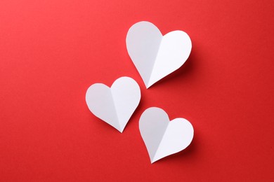 White paper hearts on red background, flat lay