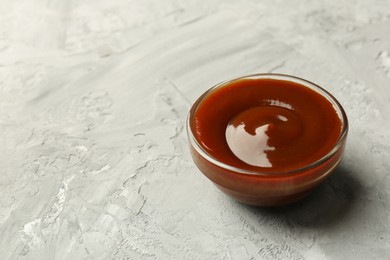 Photo of Tasty barbeque sauce in bowl on grey textured table, closeup. Space for text