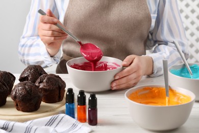 Woman mixing cream with pink food coloring at white wooden table, closeup. Decorate cupcakes