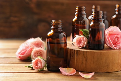 Photo of Bottles of rose essential oil and fresh flowers on wooden table, space for text