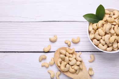 Photo of Tasty cashew nuts and green leaves on white wooden table, flat lay. Space for text