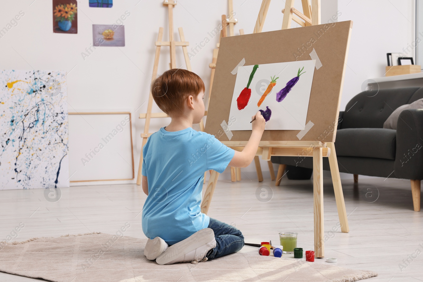 Photo of Little boy painting in studio. Using easel to hold canvas