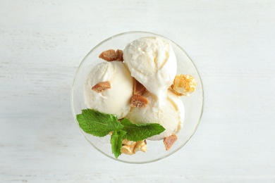 Photo of Delicious ice cream with caramel candies and popcorn in dessert bowl on white wooden table, top view