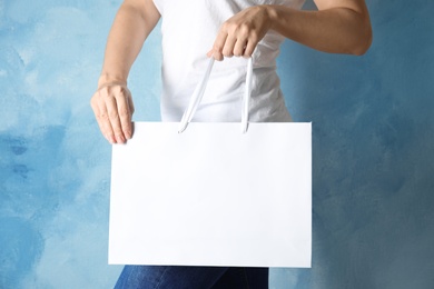 Woman holding mock-up of paper shopping bag on color background