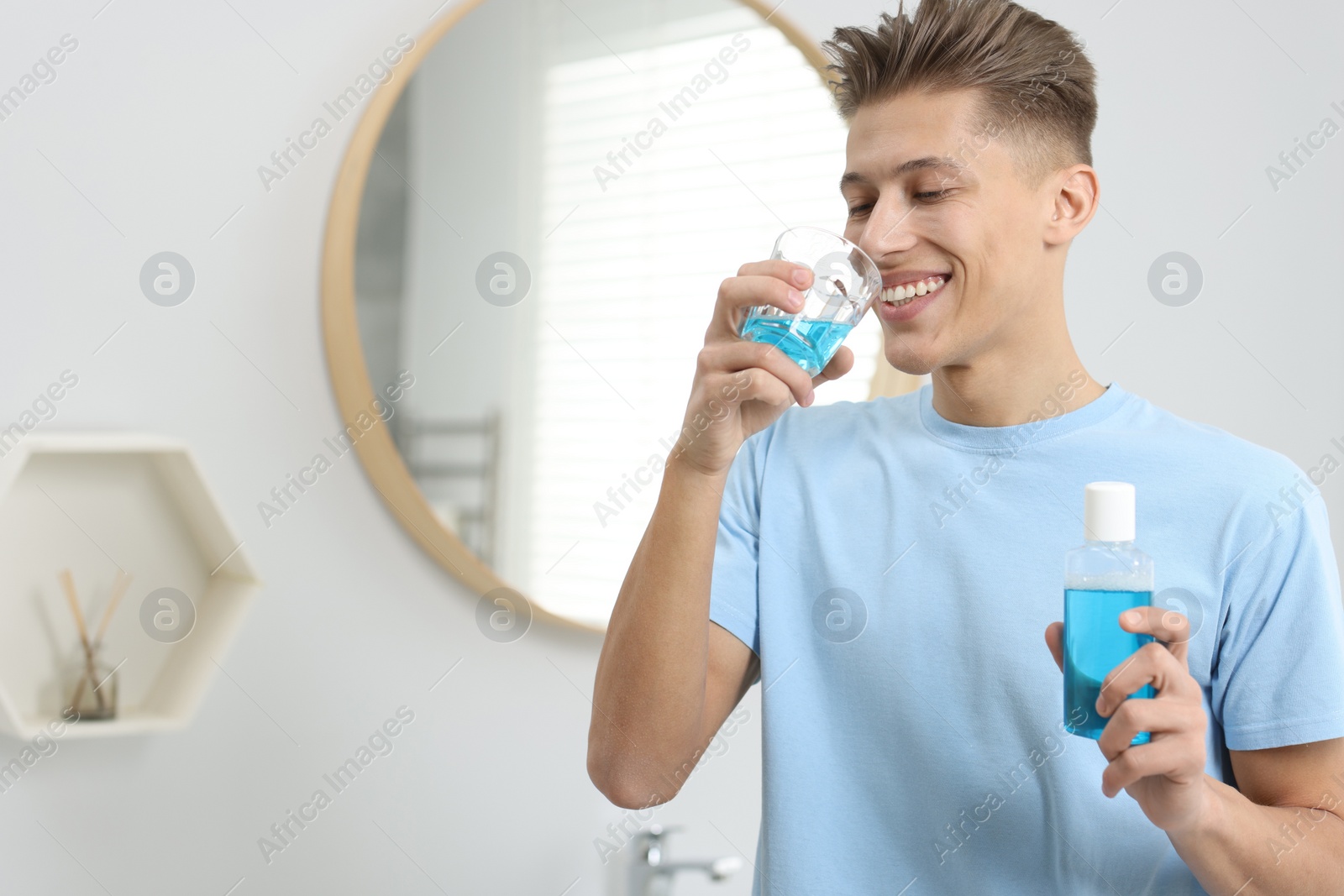 Photo of Young man using mouthwash in bathroom. Oral hygiene