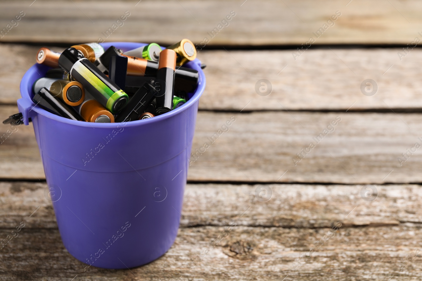 Image of Used batteries in bucket on wooden table, space for text