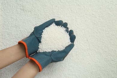 Photo of Woman holding pile of granular mineral fertilizer over grains, top view