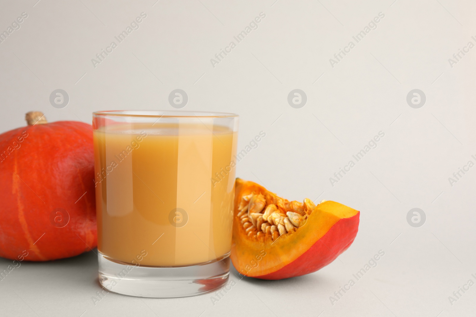 Photo of Tasty pumpkin juice in glass, whole and cut pumpkins on light background. Space for text