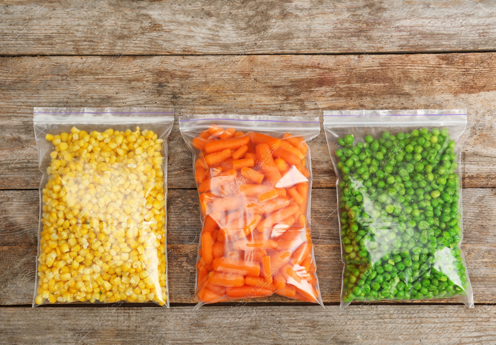Photo of Plastic bags with frozen vegetables on wooden background, top view
