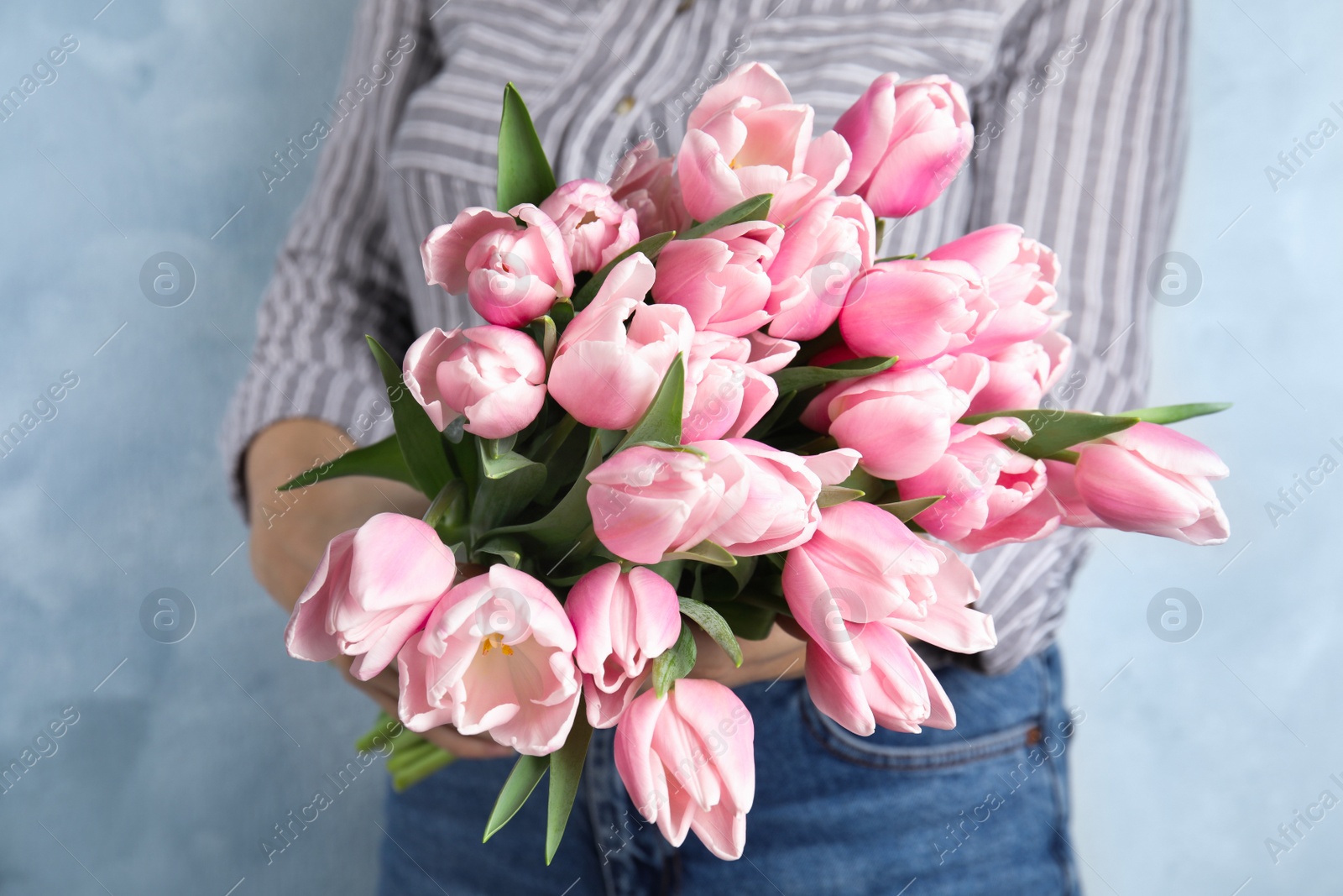 Photo of Woman with beautiful pink spring tulips on light blue background, closeup