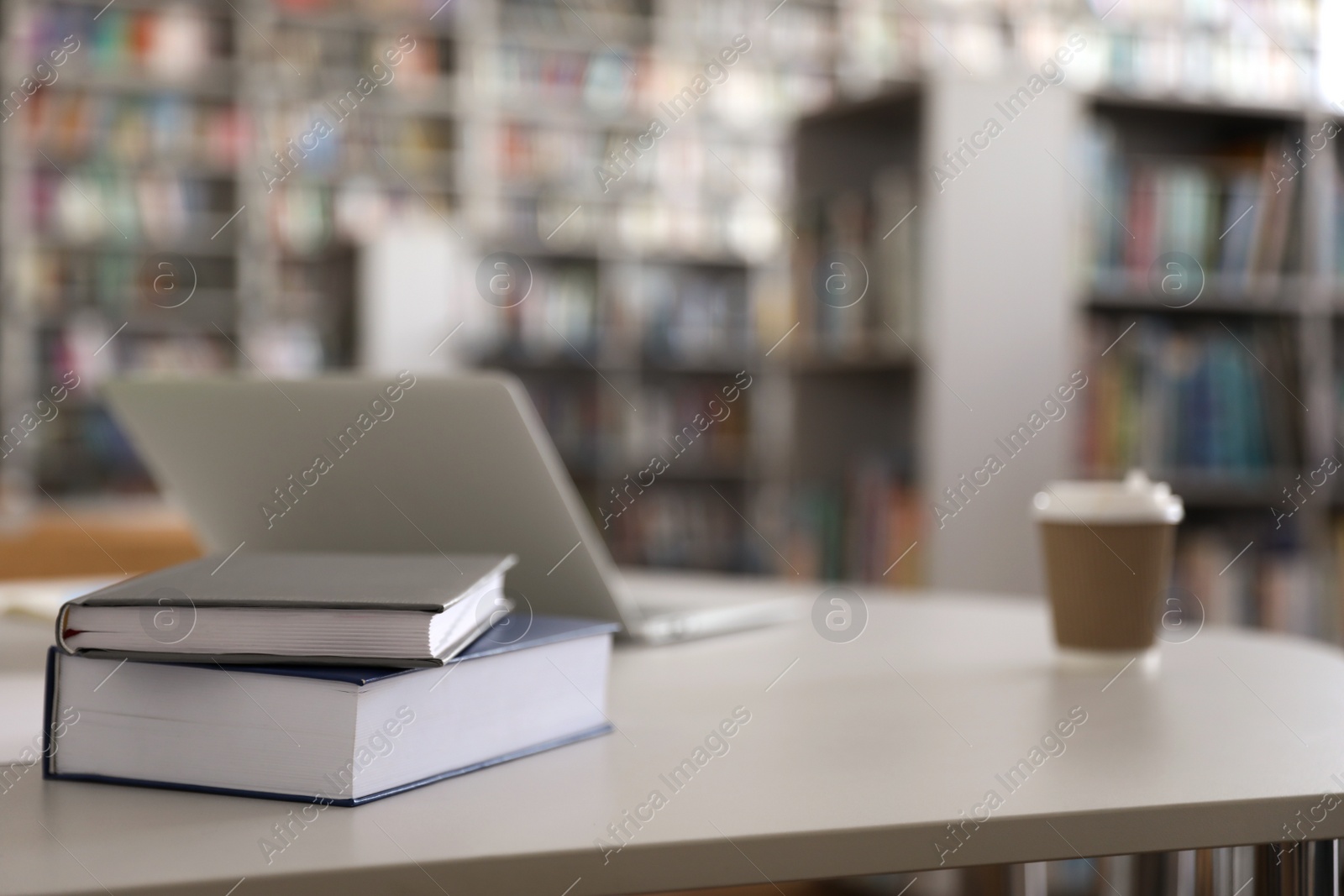 Photo of Books, laptop and drink on table in library