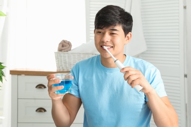 Photo of Man brushing teeth and holding glass with mouthwash in bathroom
