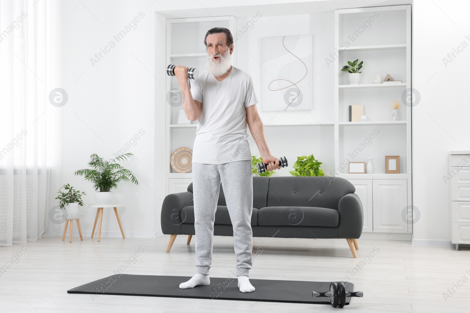 Photo of Senior man exercising with dumbbells on mat at home. Sports equipment