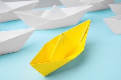Photo of Yellow paper boat among others on light blue background, closeup. Uniqueness concept