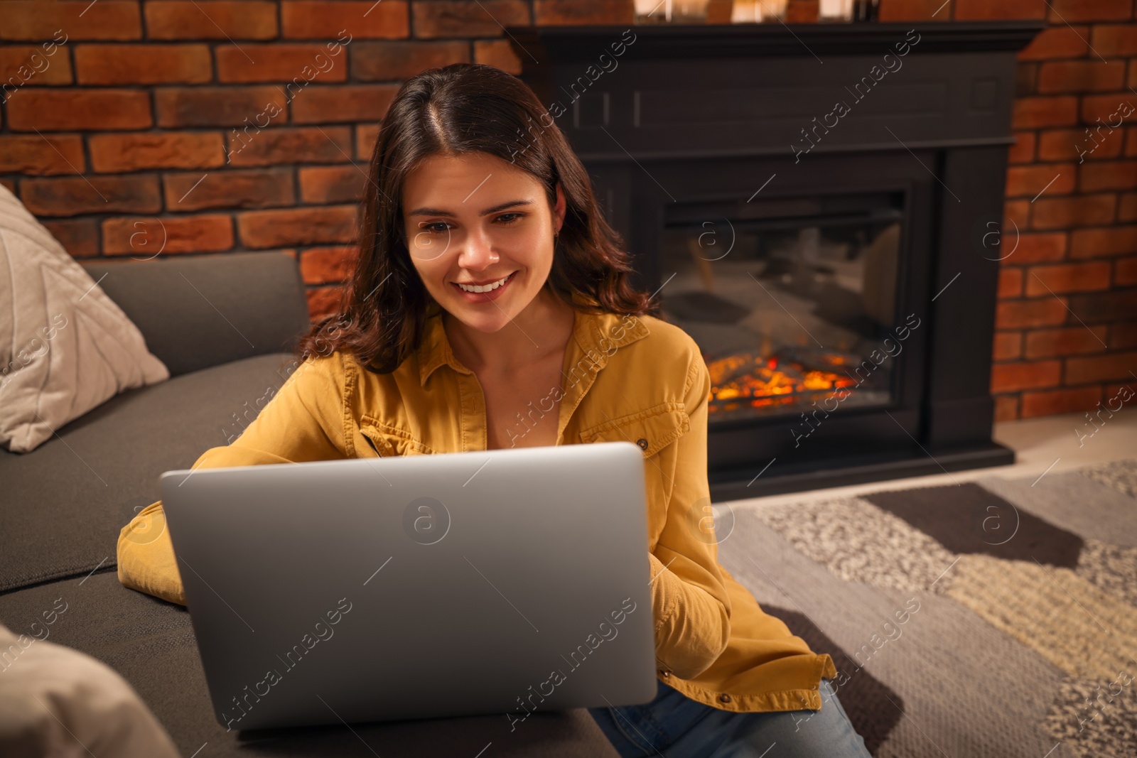 Photo of Young woman with laptop on floor near fireplace at home