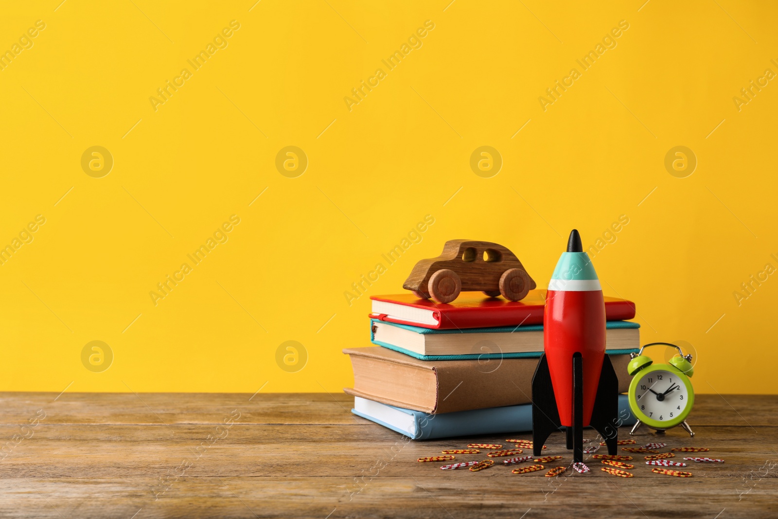 Photo of Bright toy rocket and school supplies on wooden desk. Space for text