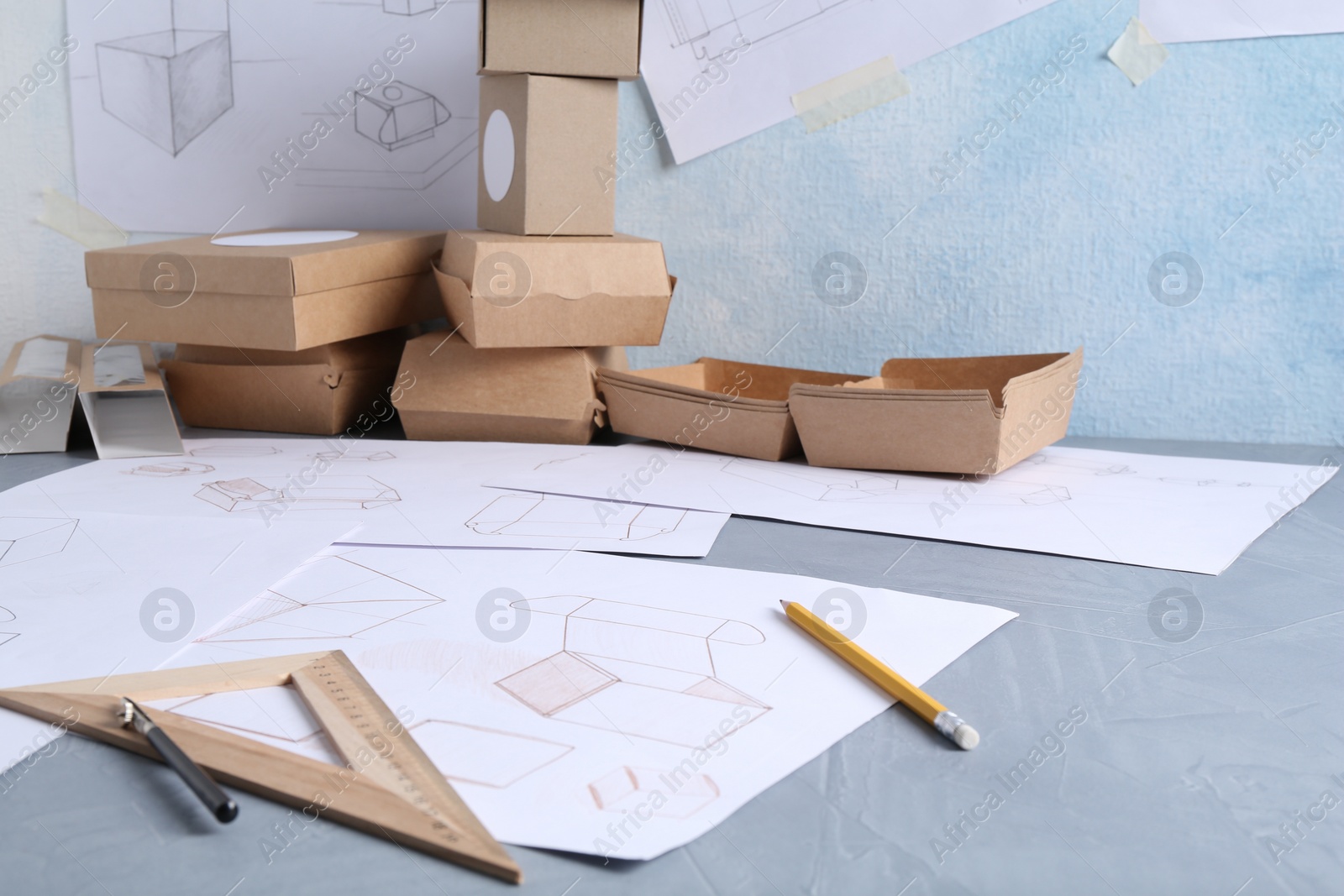 Photo of Creating packaging design. Drawings, boxes and stationery on blue textured table, closeup