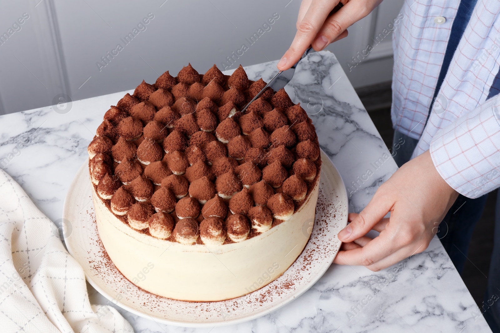 Photo of Woman cutting delicious tiramisu cake at white marble table, closeup