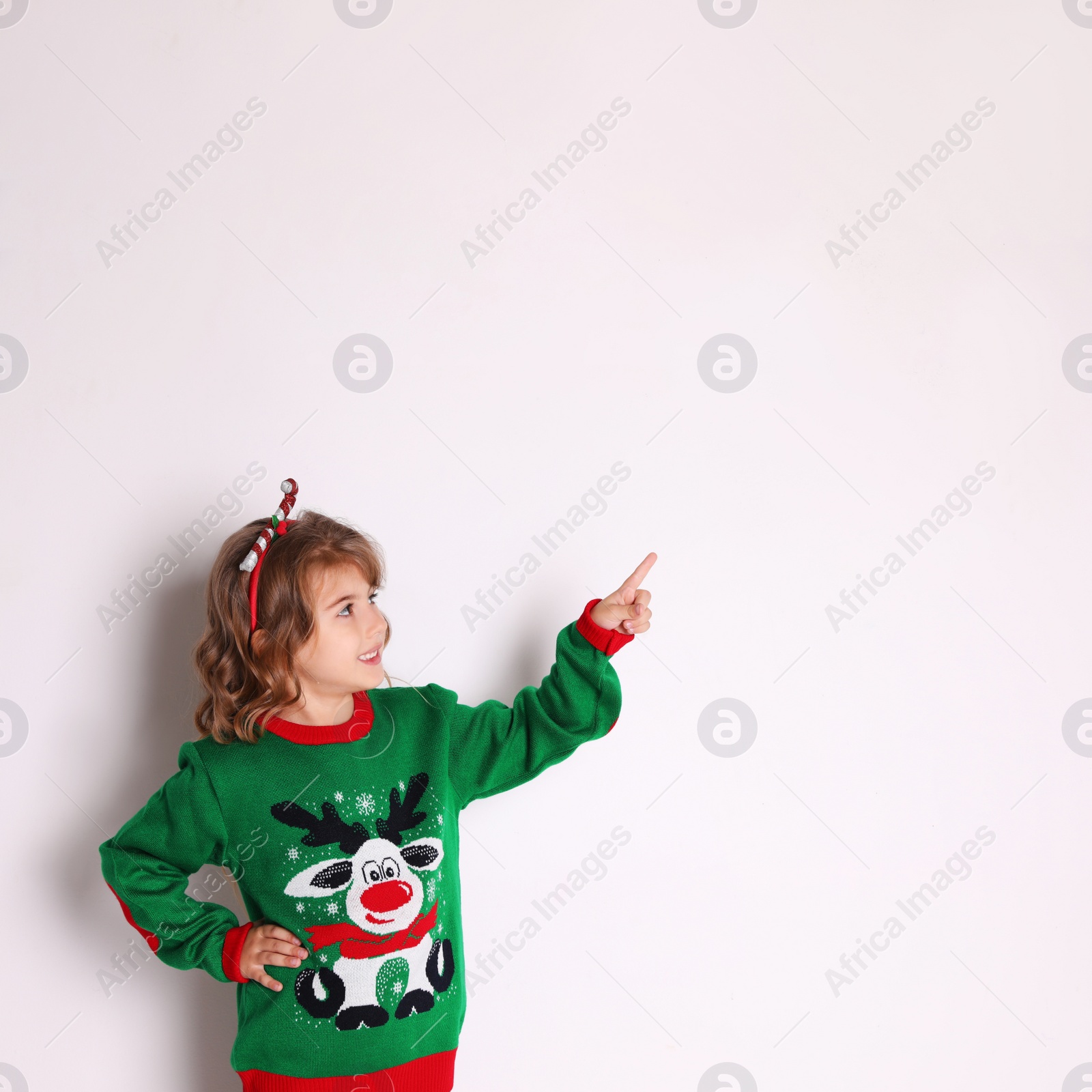 Photo of Cute little girl in green Christmas sweater pointing against white background