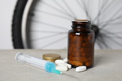 Photo of Pills and syringe on light grey table near bike wheel. Using doping in cycling sport concept