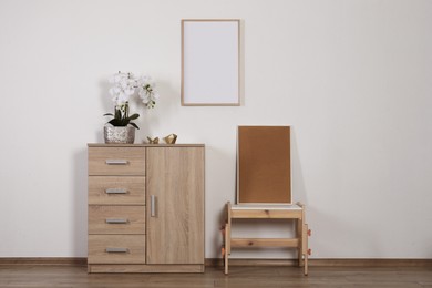 Chest of drawers, table, orchid and picture frames indoors. Interior design