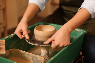 Photo of Clay crafting. Woman removing bowl from potter's wheel with thread