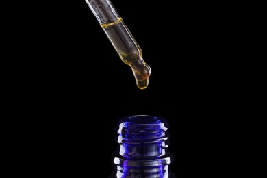 Photo of Dripping tincture from pipette into bottle on dark background, closeup