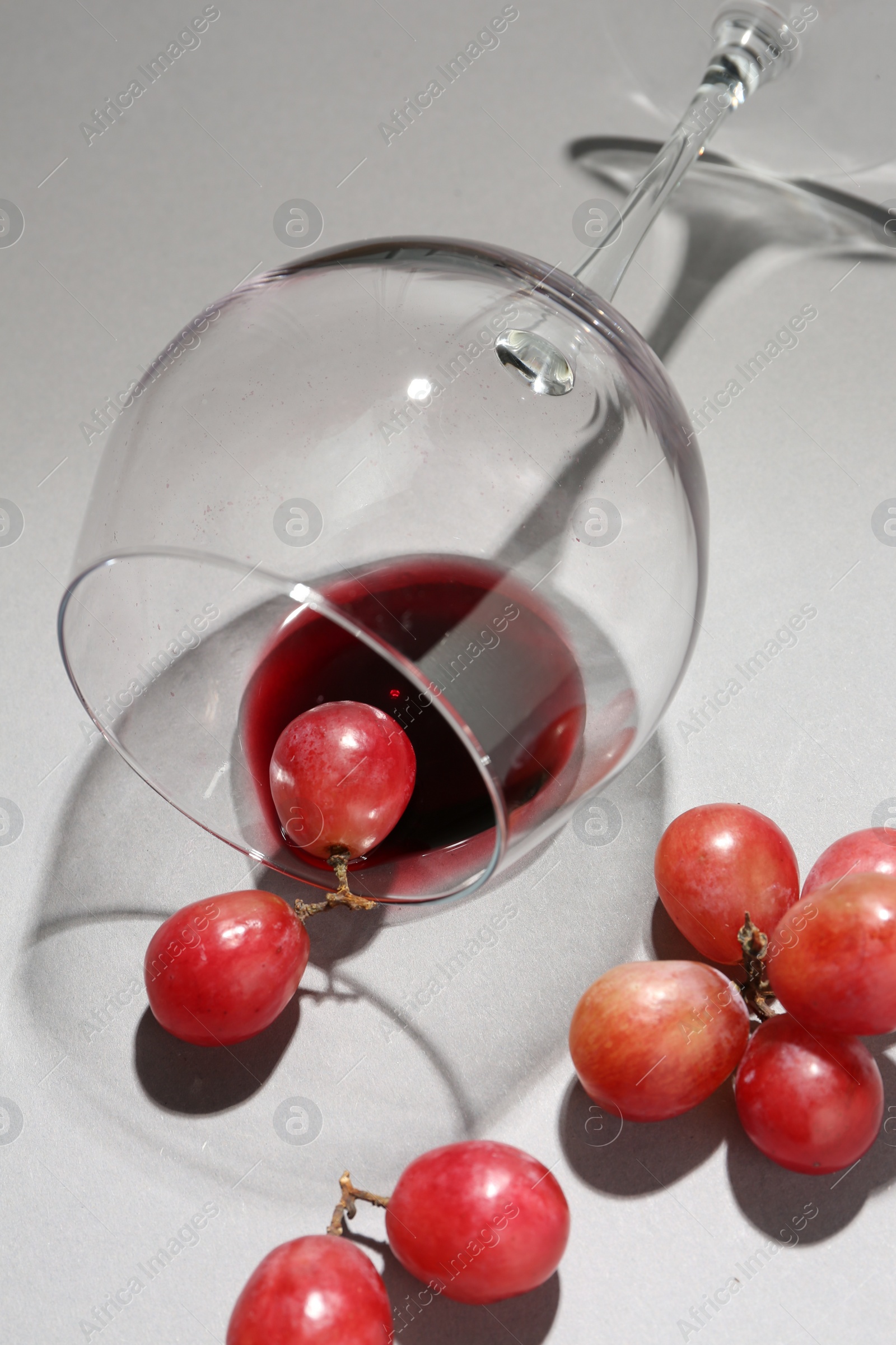 Photo of Overturned glass of wine and grapes on white background, closeup