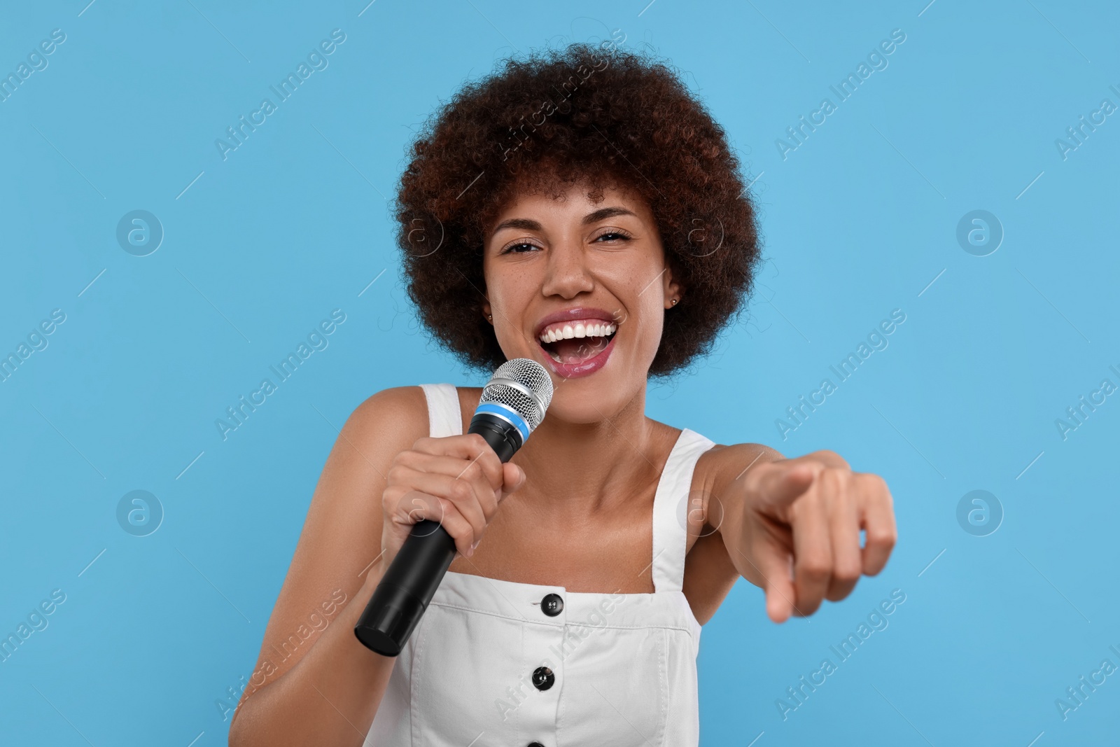 Photo of Curly young woman with microphone singing on light blue background