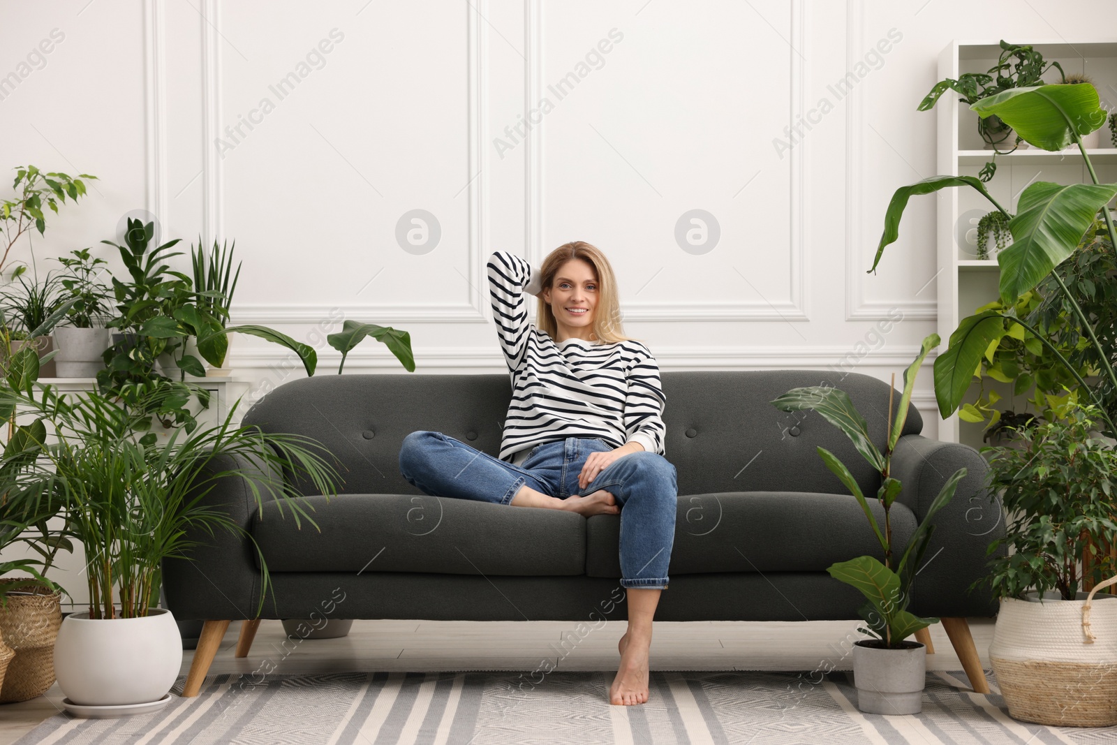 Photo of Woman relaxing on sofa surrounded by beautiful potted houseplants at home