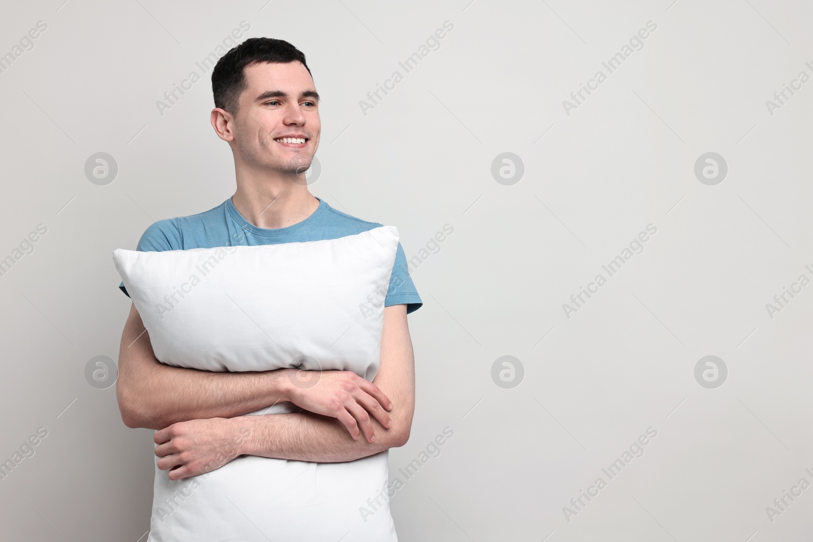 Photo of Happy man in pyjama holding pillow on light grey background, space for text