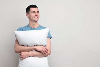 Photo of Happy man in pyjama holding pillow on light grey background, space for text