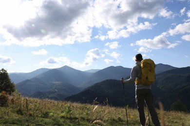 Photo of Tourist with backpack and trekking poles enjoying mountain landscape, back view. Space for text