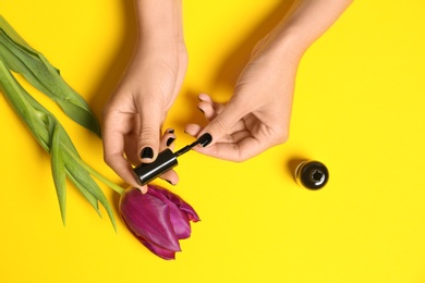 Woman applying nail polish at flower on color background, closeup