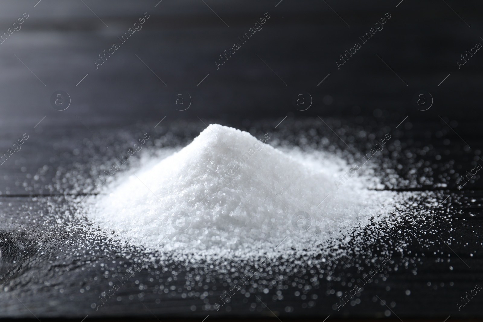 Photo of Pile of organic salt on black wooden table, closeup