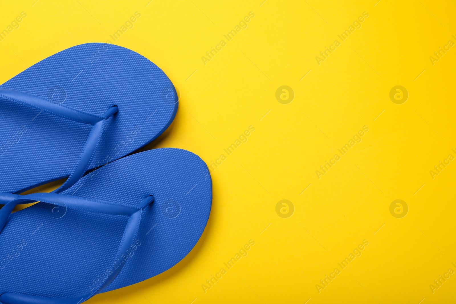 Photo of Stylish blue flip flops on yellow background, top view. Space for text