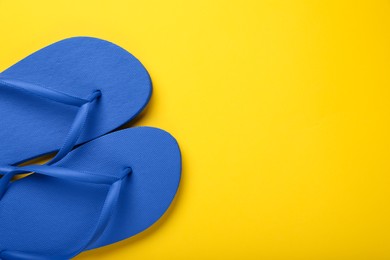 Stylish blue flip flops on yellow background, top view. Space for text