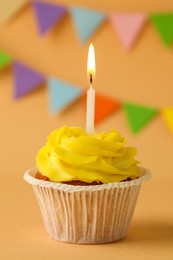 Photo of Tasty birthday cupcake with candle on orange table against party flags, closeup