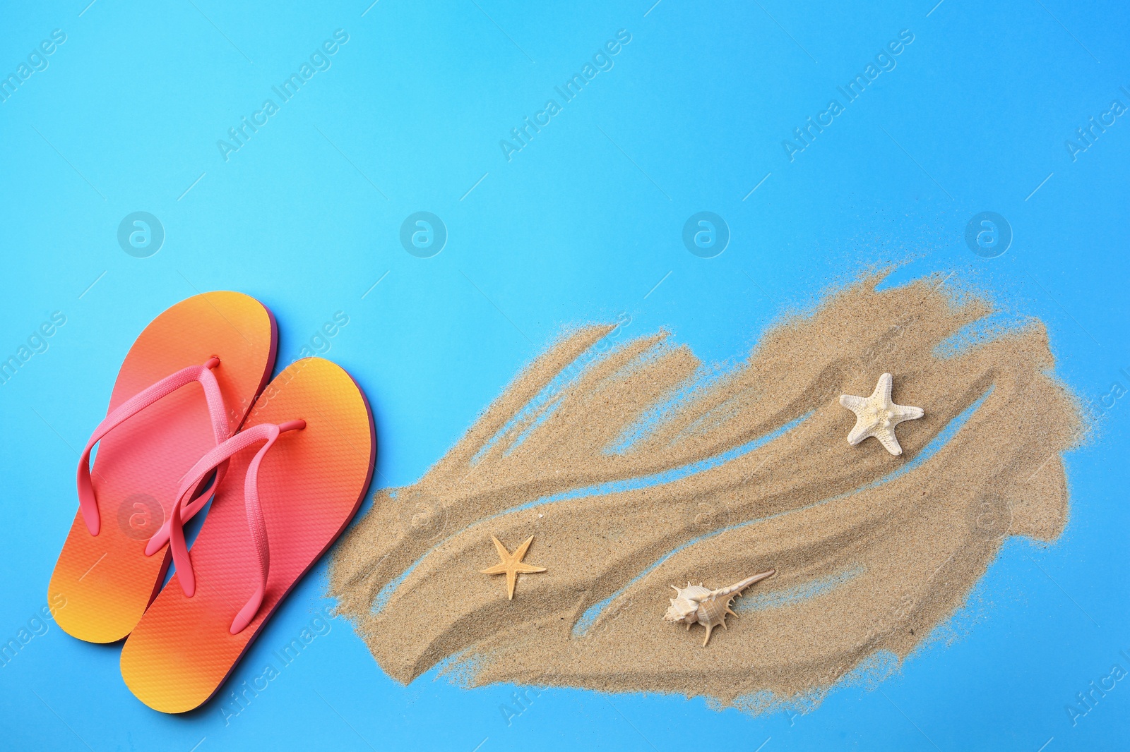 Photo of Flip flops and sand on light blue background, flat lay with space for text. Beach accessories